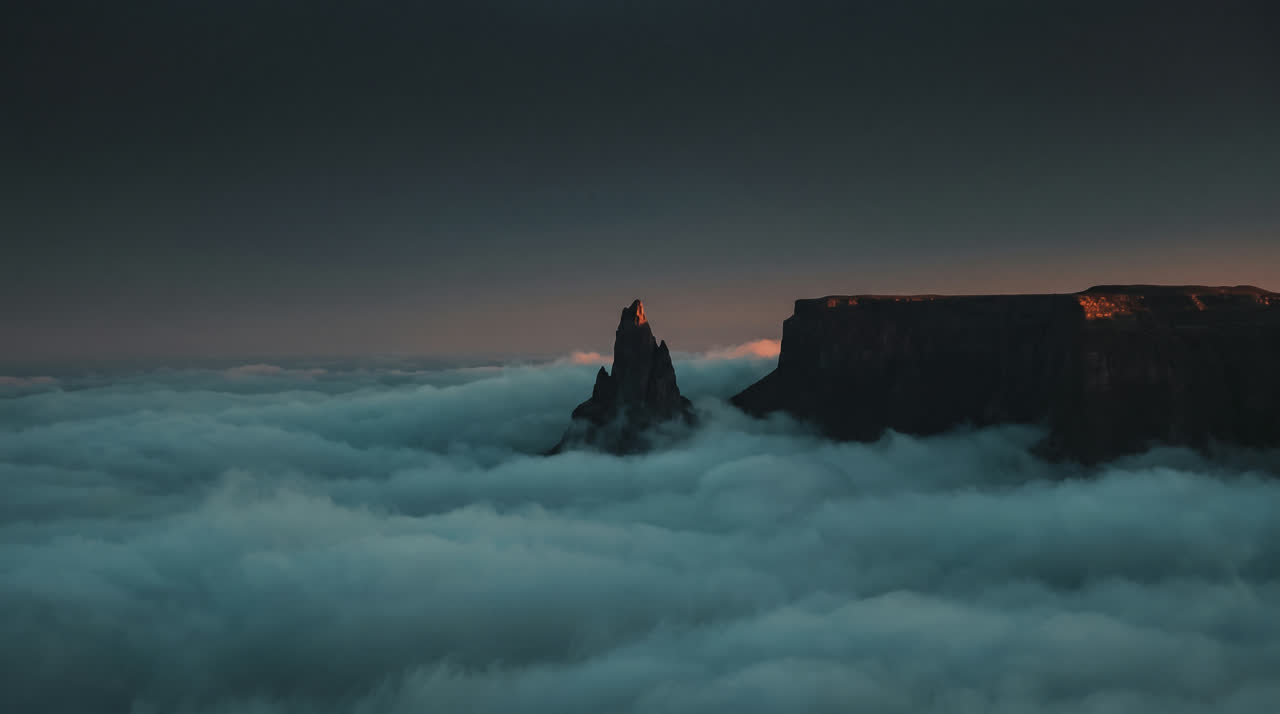 A sharp needle-like mountain peak next to a flat-topped plateau above the clouds